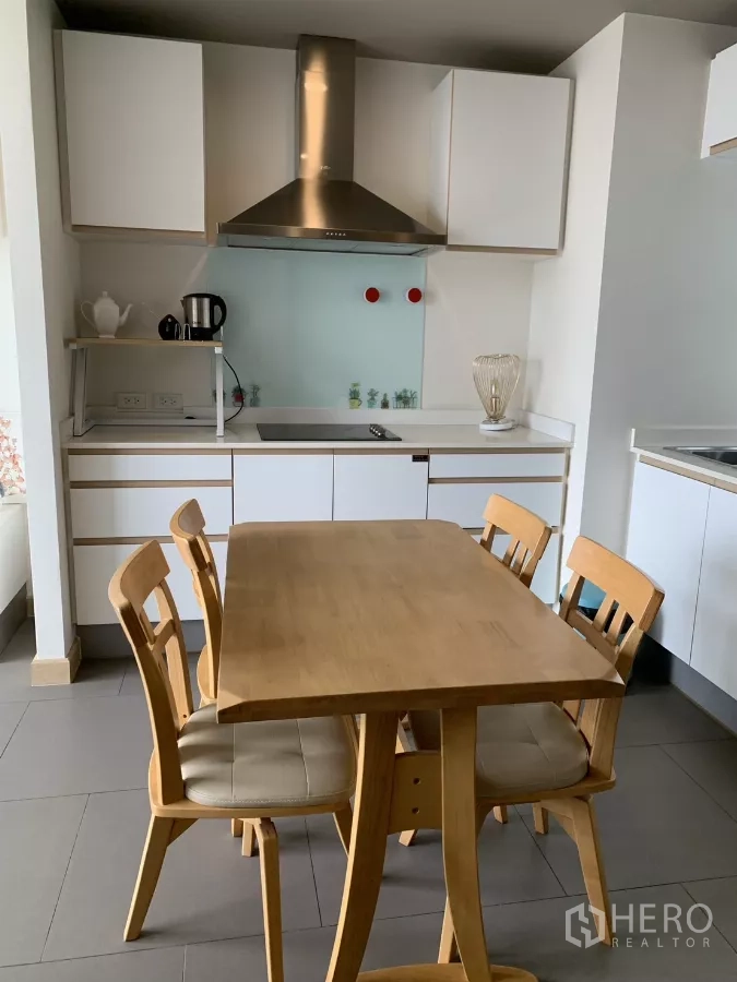 公寓 出租在Watthana, Bangkok - 现代小厨房，电磁炉与不锈钢烟机，木质餐桌四椅