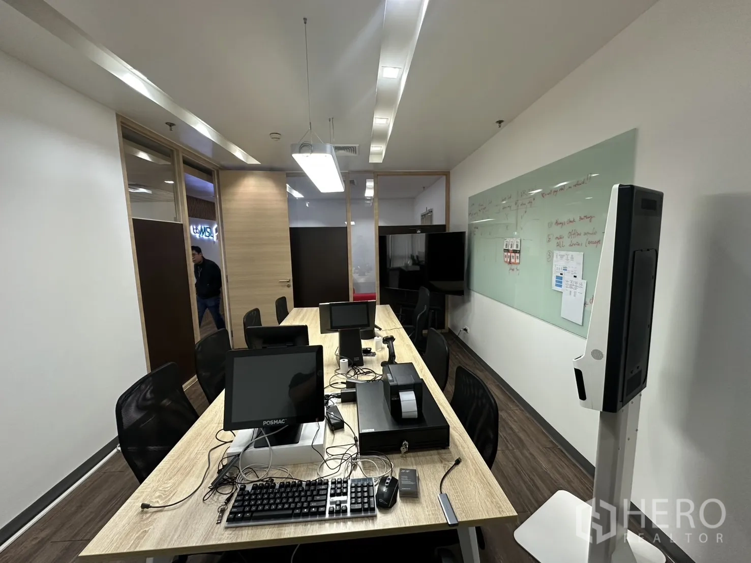 Office Space for rent - Corridor view of meeting room with long table and glass whiteboard.
