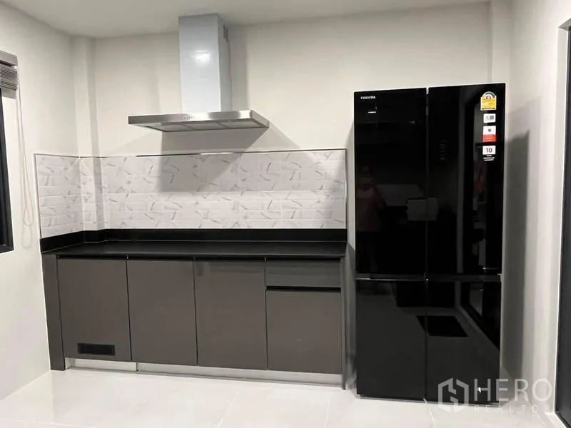 Detached House for rent - Sleek kitchen with extractor hood, glossy cabinets and a black double-door refrigerator.