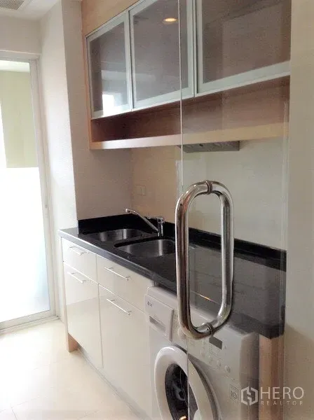 คอนโด ให้เช่าหรือขายในWatthana, Bangkok - ครัวกะทัดรัด ท็อปหินสีดำ อ่างล้างจาน ตู้แขวน และเครื่องซักผ้าหลังบานกระจก