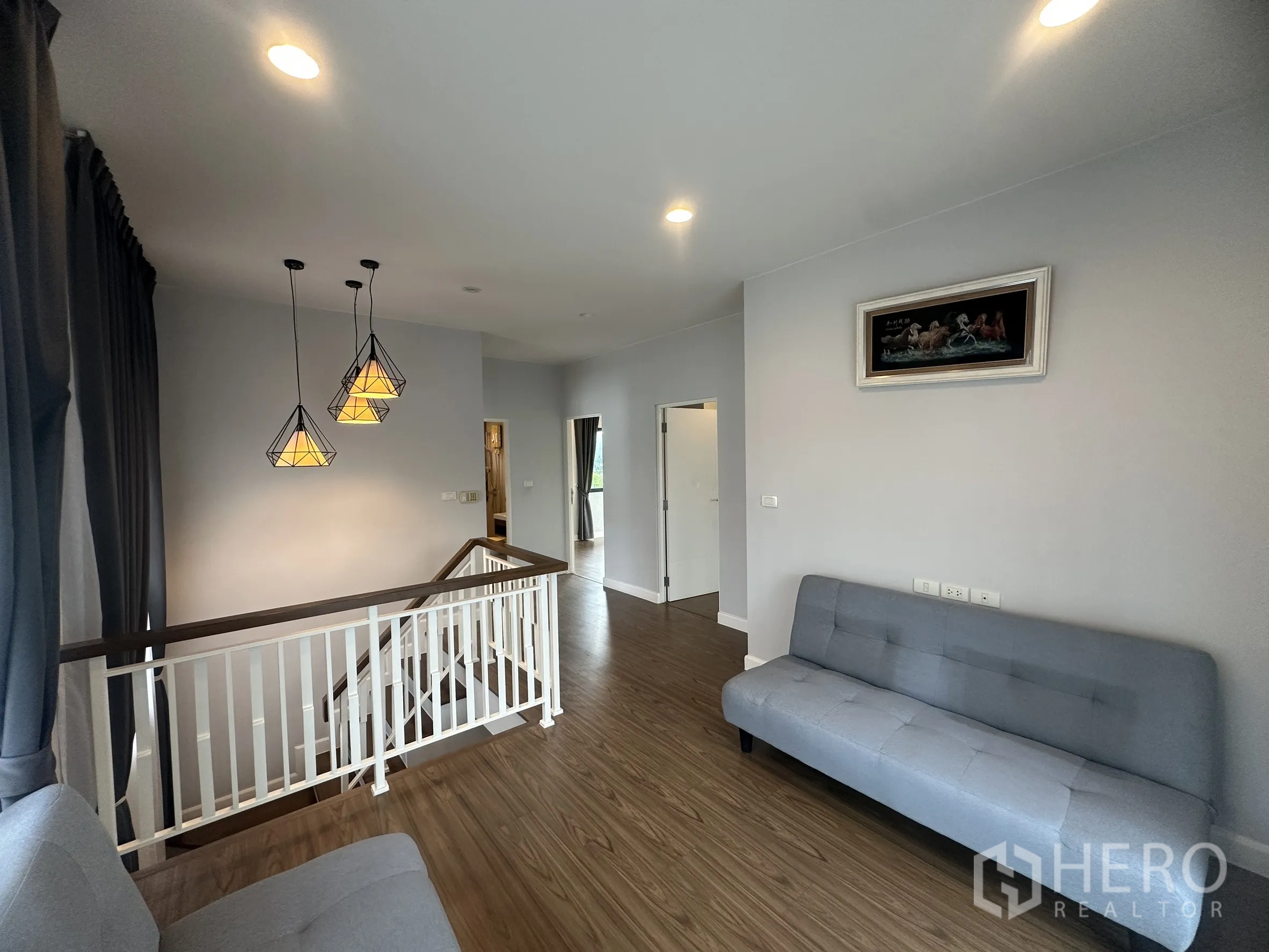 独栋房屋 for rent or sale in Lam Luk Ka, Pathum Thani - 二楼过道休闲区，吊灯、楼梯与沙发座。