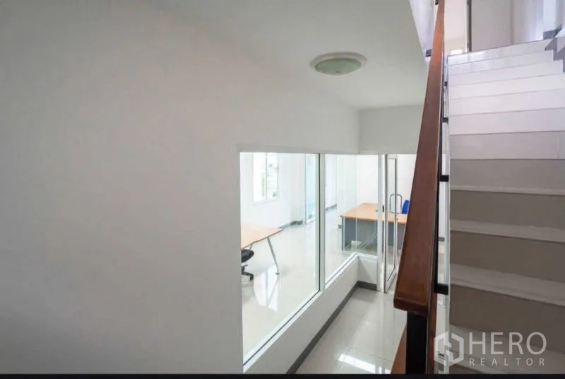 Home Office for rent or sale in Lat Krabang, Bangkok - Stairwell with metal handrail beside interior windows overlooking offices.