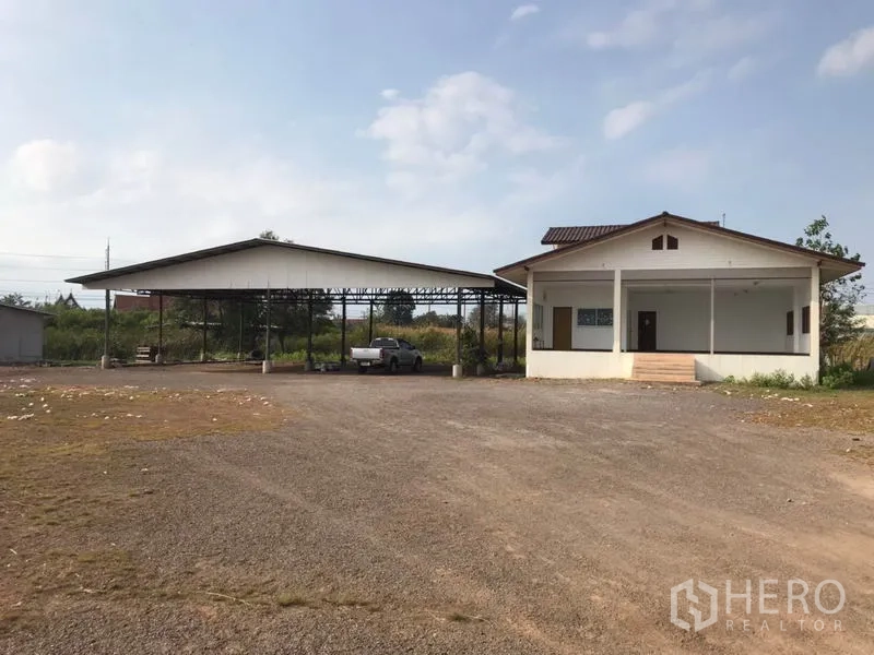 Land for sale in Mueang Samut Sakhon, Samut Sakhon - Expansive roadside land with open steel‑roof shed and single‑storey office on a gravel yard.