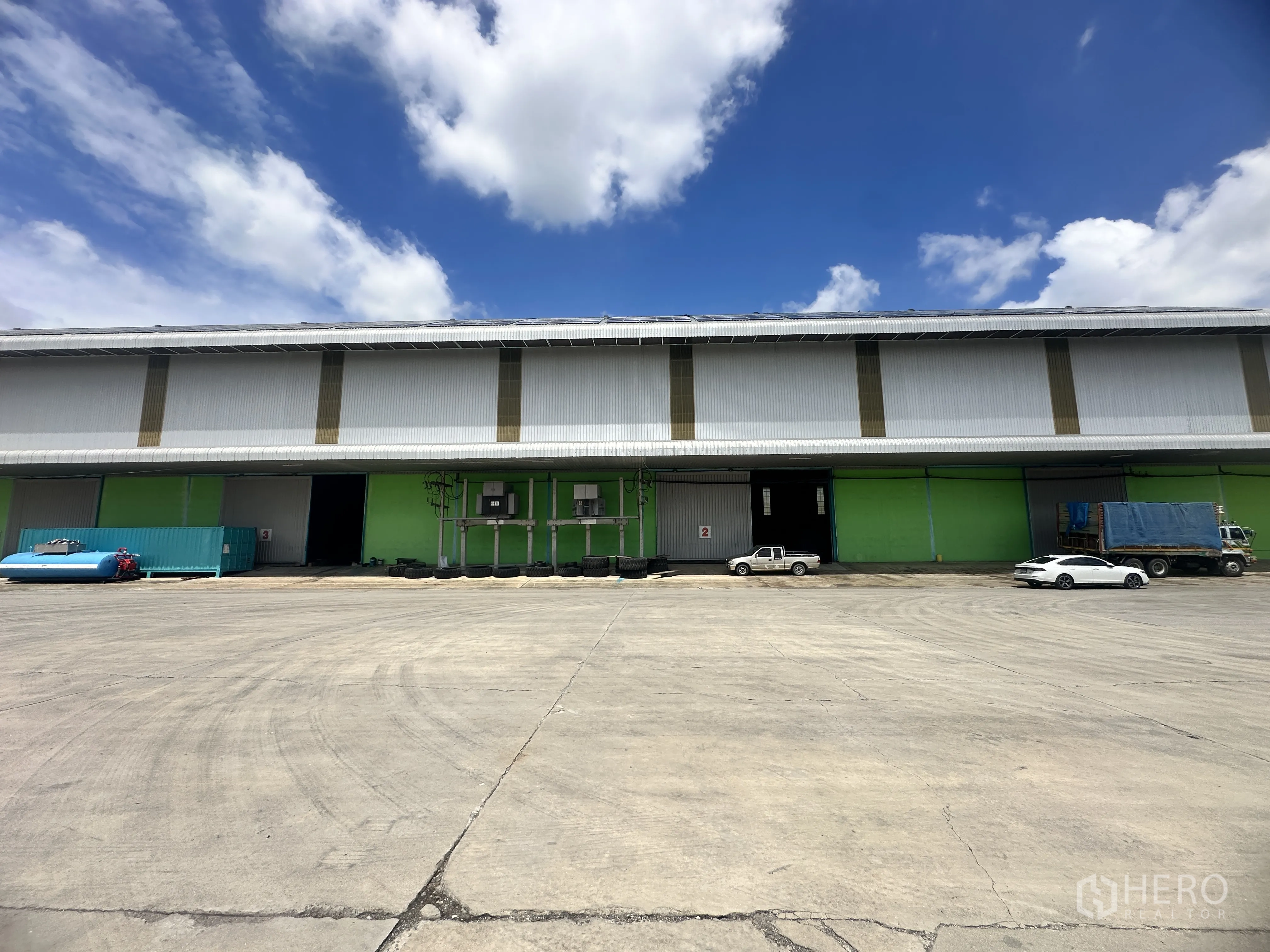 仓库 for rent in Sai Noi, Nonthaburi - 仓库正立面，多个装卸口，前方是宽阔硬化场地与车辆。