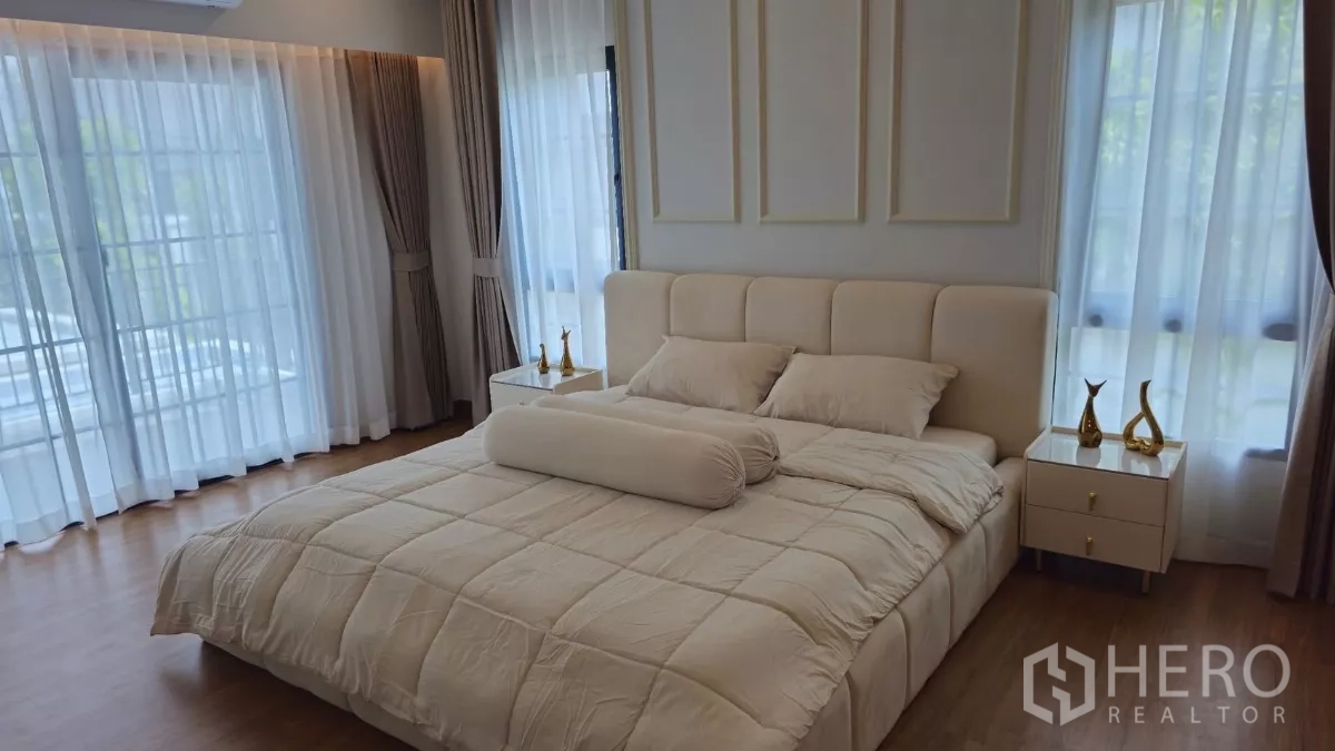 Detached House for rent or sale in Bang Phli, Samut Prakan - Sunlit bedroom with king bed, tall windows and sliding doors with sheer curtains.