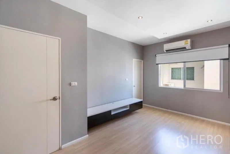 Townhouse for rent or sale in Watthana, Bangkok - Air‑conditioned room with window and roller blind over wood flooring.