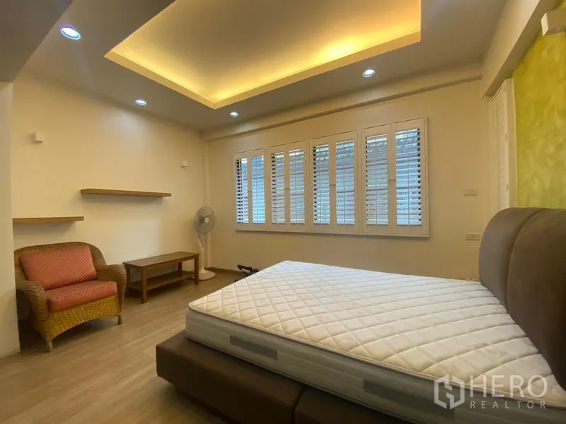Detached House for sale in Khlong Toei, Bangkok - Spacious bedroom with cove-lit ceiling, window shutters, and upholstered bed.