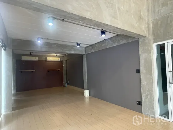 Home Office for rent in Suan Luang, Bangkok - Open studio room with track lighting, gray feature wall, and wood-style flooring.