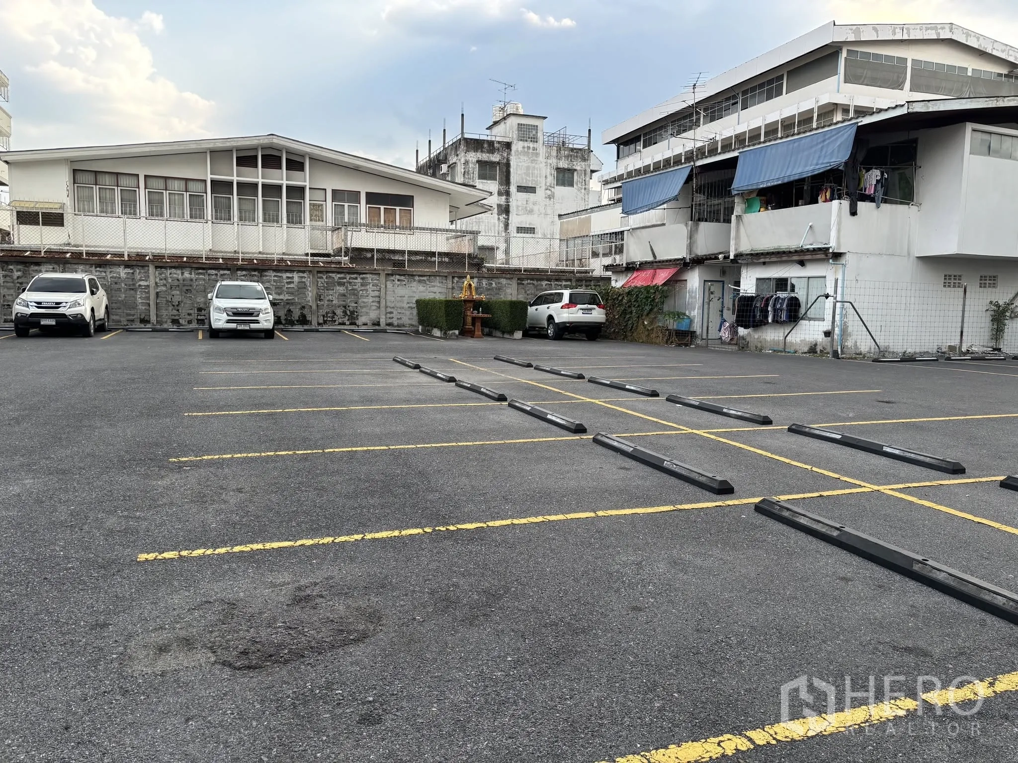 Land for rent in Sathon, Bangkok - Open parking area with wheel stops, painted lines, and a boundary wall with nearby houses.