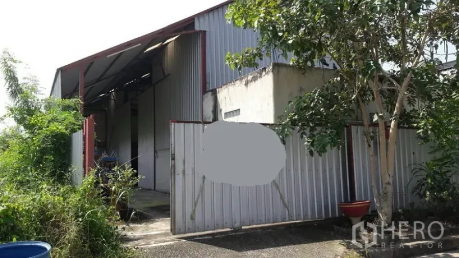 货栈 出售在Pathum Thani - 仓库正面，波纹金属大门与入口处的树荫。