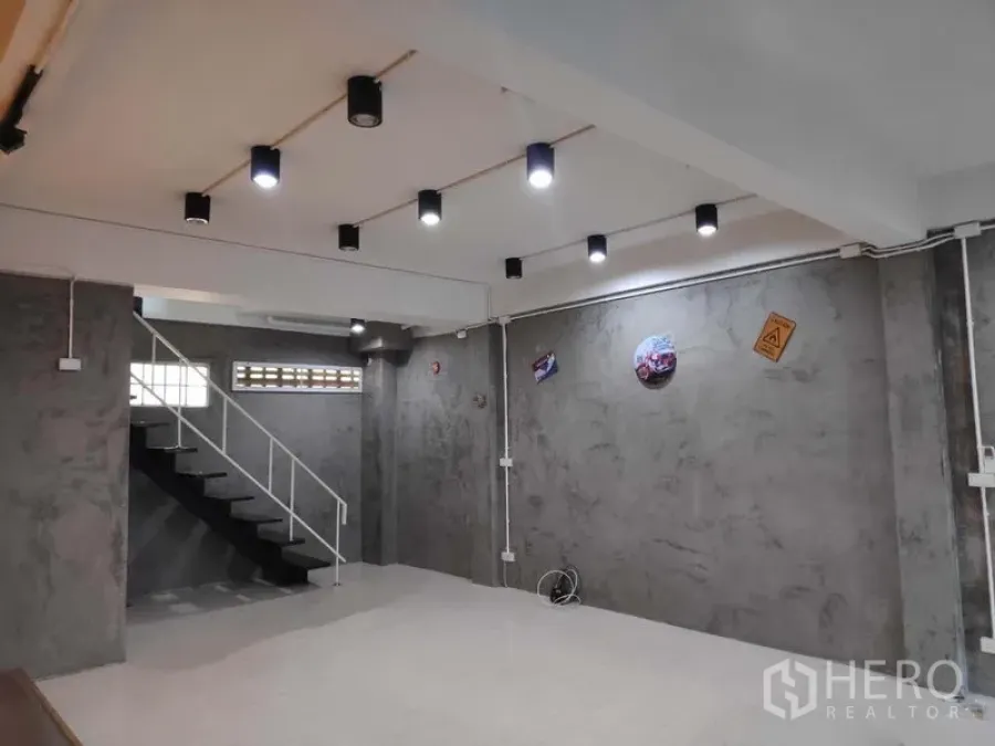 Home Office for rent in Khlong Toei, Bangkok - Open-plan ground floor with polished concrete walls, ceiling spotlights, and a metal staircase.