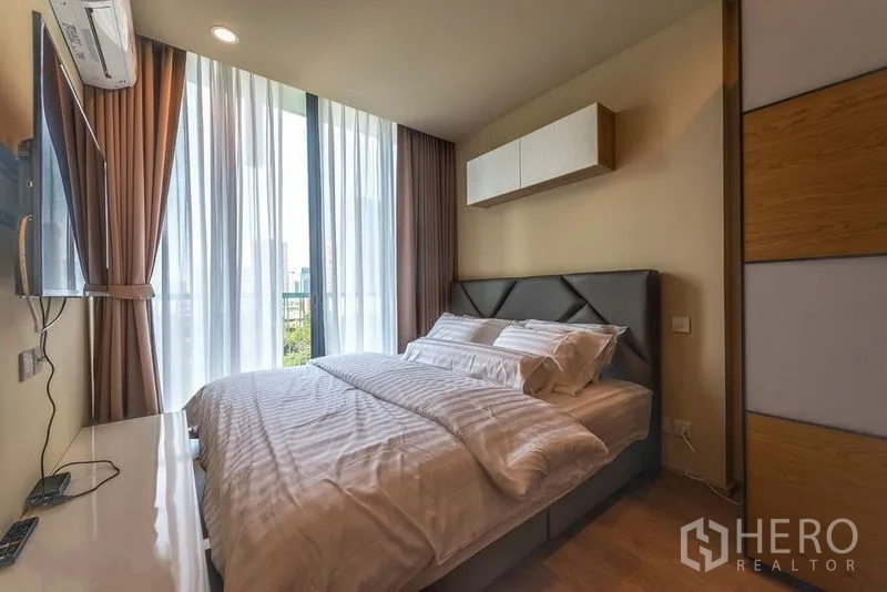 Condominium for rent in Watthana, Bangkok - Bedroom with sheer curtains, overhead storage and balcony-height windows.