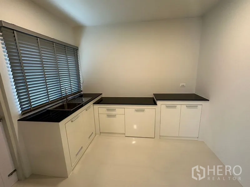 Detached House for rent in Bang Phli, Samut Prakan - Fitted kitchen with black stone countertops, white cabinets and window blinds.