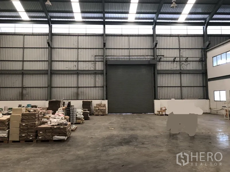 Factory for rent in Khlong Luang, Pathum Thani - Central loading area facing a tall roller shutter, high clerestory windows and open floor space.