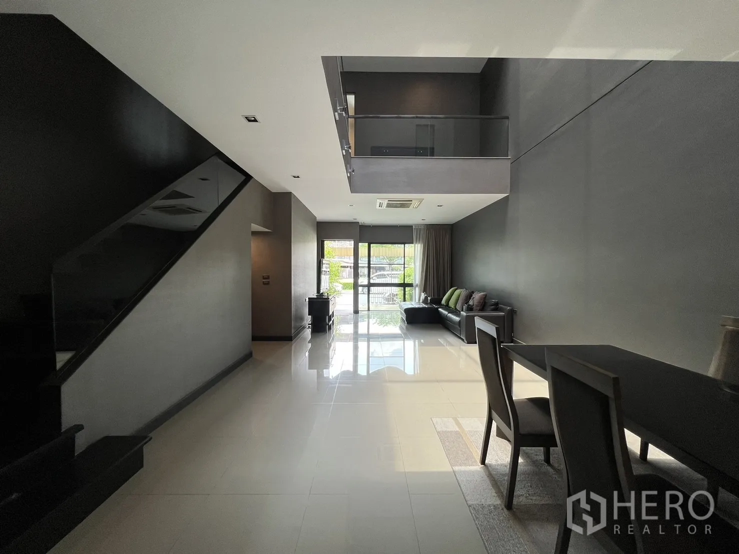 联排别墅 出租在Lat Phrao, Bangkok - 從餐區望向入口的長型起居空間，樓梯與高天花設計。