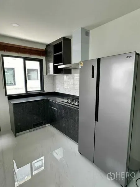 独立式住宅 出租在Bang Phli, Samut Prakan - L形厨房，黑色橱柜，燃气灶与烟机，高大不锈钢冰箱。