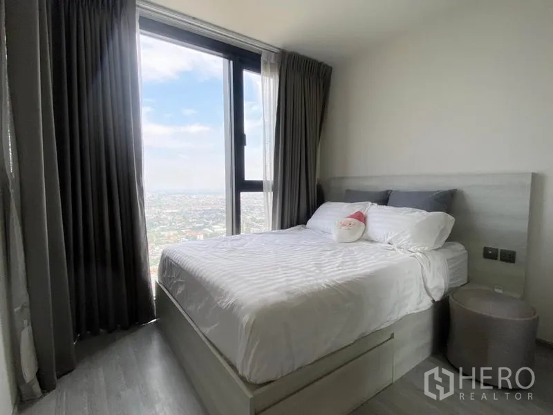 Condominium for rent in Phra Khanong, Bangkok - Bedroom with large window, city view and double bed dressed in white linens.