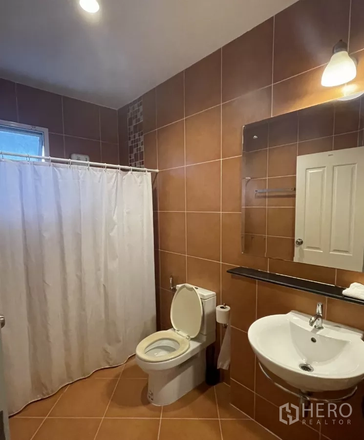บ้าน ขายในMin Buri, Bangkok - ห้องน้ำปูกระเบื้องสีน้ำตาล มีม่านอาบน้ำ อ่างล้างหน้าและโถสุขภัณฑ์