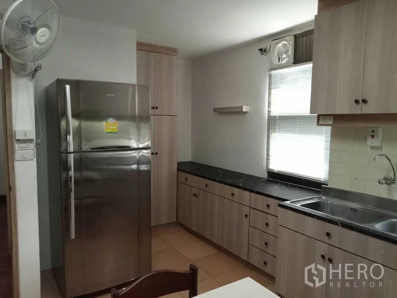 Condominium for rent in Watthana, Bangkok - Kitchen view showing stainless-steel refrigerator, sink and dark countertops.