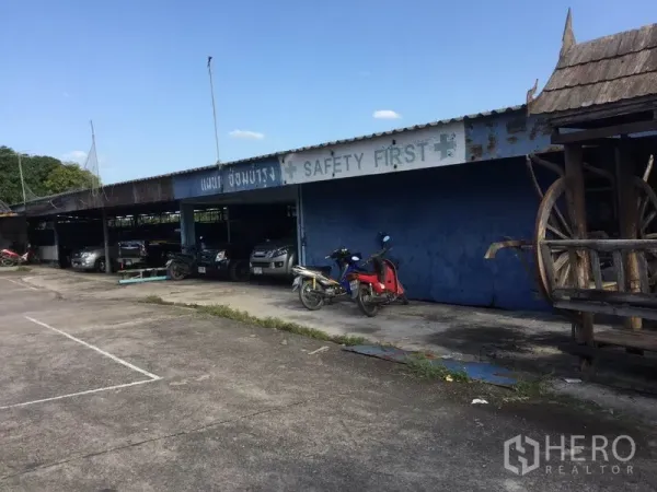 Warehouse for sale in Sai Noi, Nonthaburi - Covered parking shed with blue wall and vehicles, suitable for staff or fleet.
