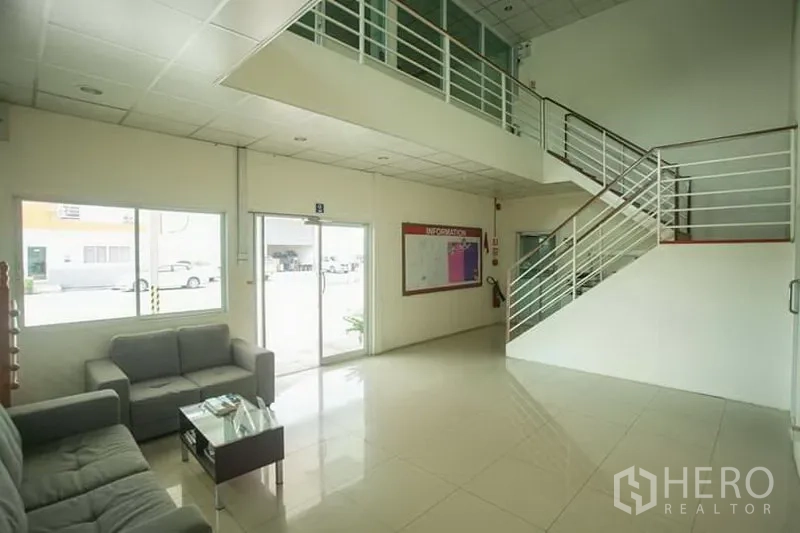 工厂 出租在Phra Nakhon Si Ayutthaya - 办公大厅整洁，瓷砖地面、玻璃入口、沙发区与通往夹层的楼梯。