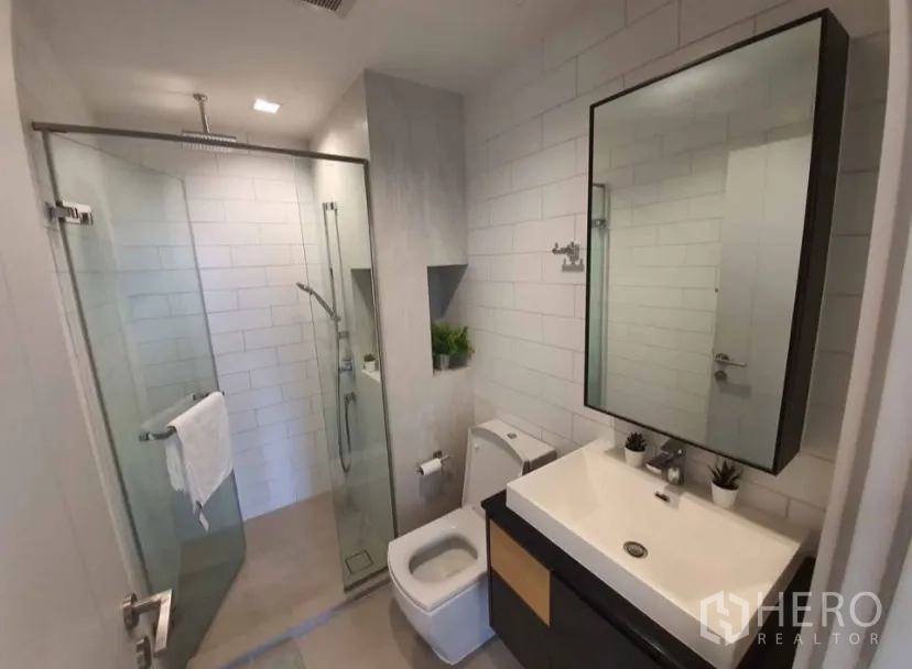 Condominium for rent in Chatuchak, Bangkok - Modern bathroom with glass-enclosed rain shower, vanity and toilet.