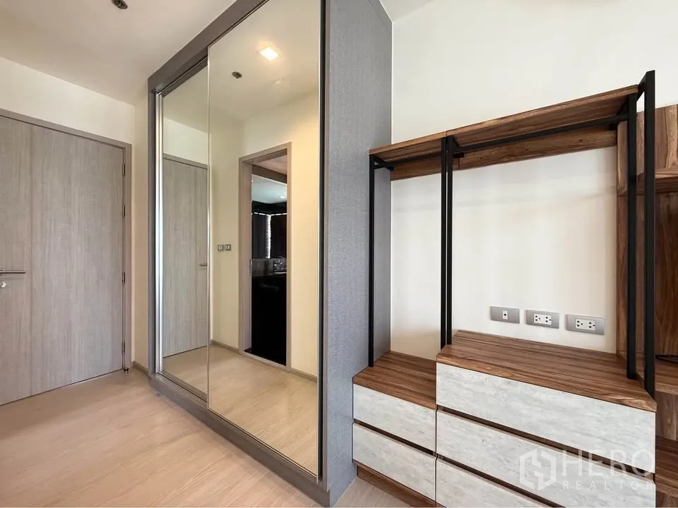 Condominium for rent in Khlong Toei, Bangkok - Entry area with mirrored wardrobe and open wood-and-metal shelving.