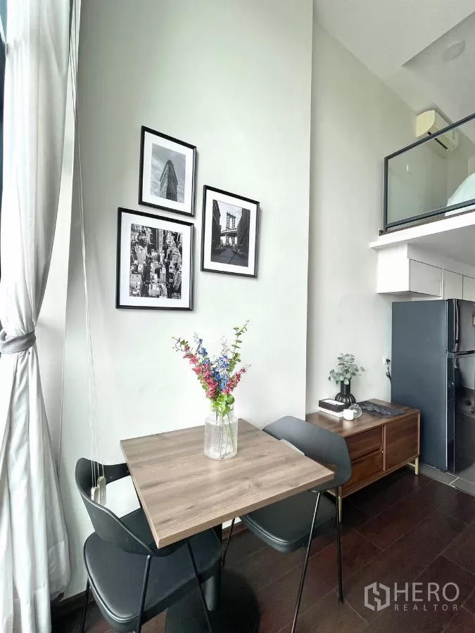 Condominium for rent in Watthana, Bangkok - Two-seat dining nook with flowers and gallery wall next to a mezzanine glass railing.