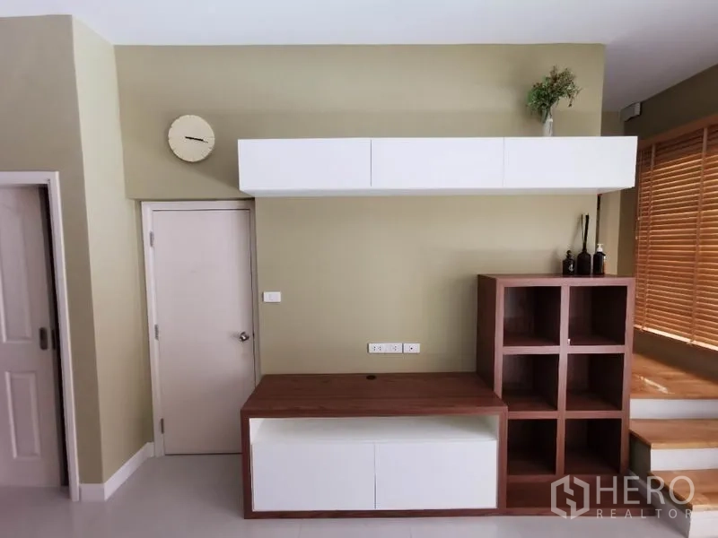 联排别墅 出租在Wang Thonglang, Bangkok - 客厅内置电视墙，白色柜体与木质格架，搭配百叶窗的现代联排别墅。