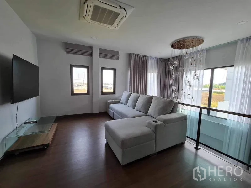 Detached House for rent or sale in Bang Phli, Samut Prakan - Upstairs family lounge with large sectional sofa, wall-mounted TV and glass balustrade.