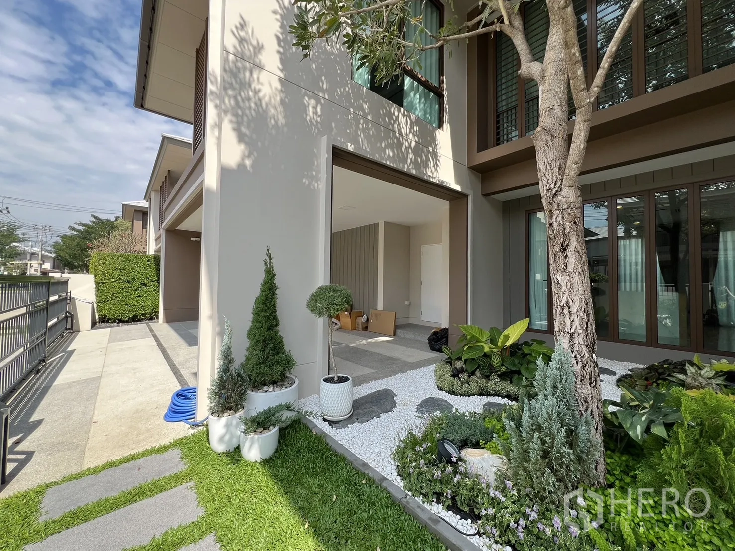 Detached House for rent or sale in Bang Kapi, Bangkok - Side view showing the carport and open-air courtyard with potted plants and lawn.