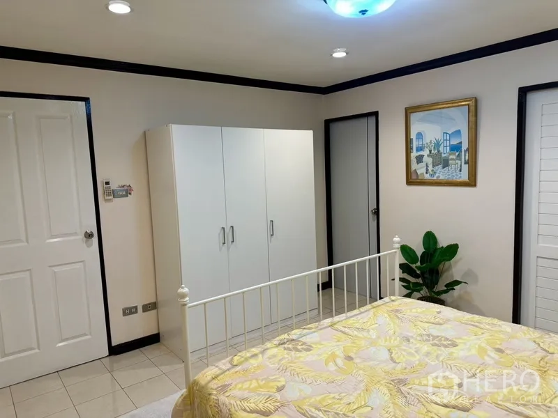 联排别墅 出租在Prawet, Bangkok - 卧室内白色衣柜、装饰画与绿植。