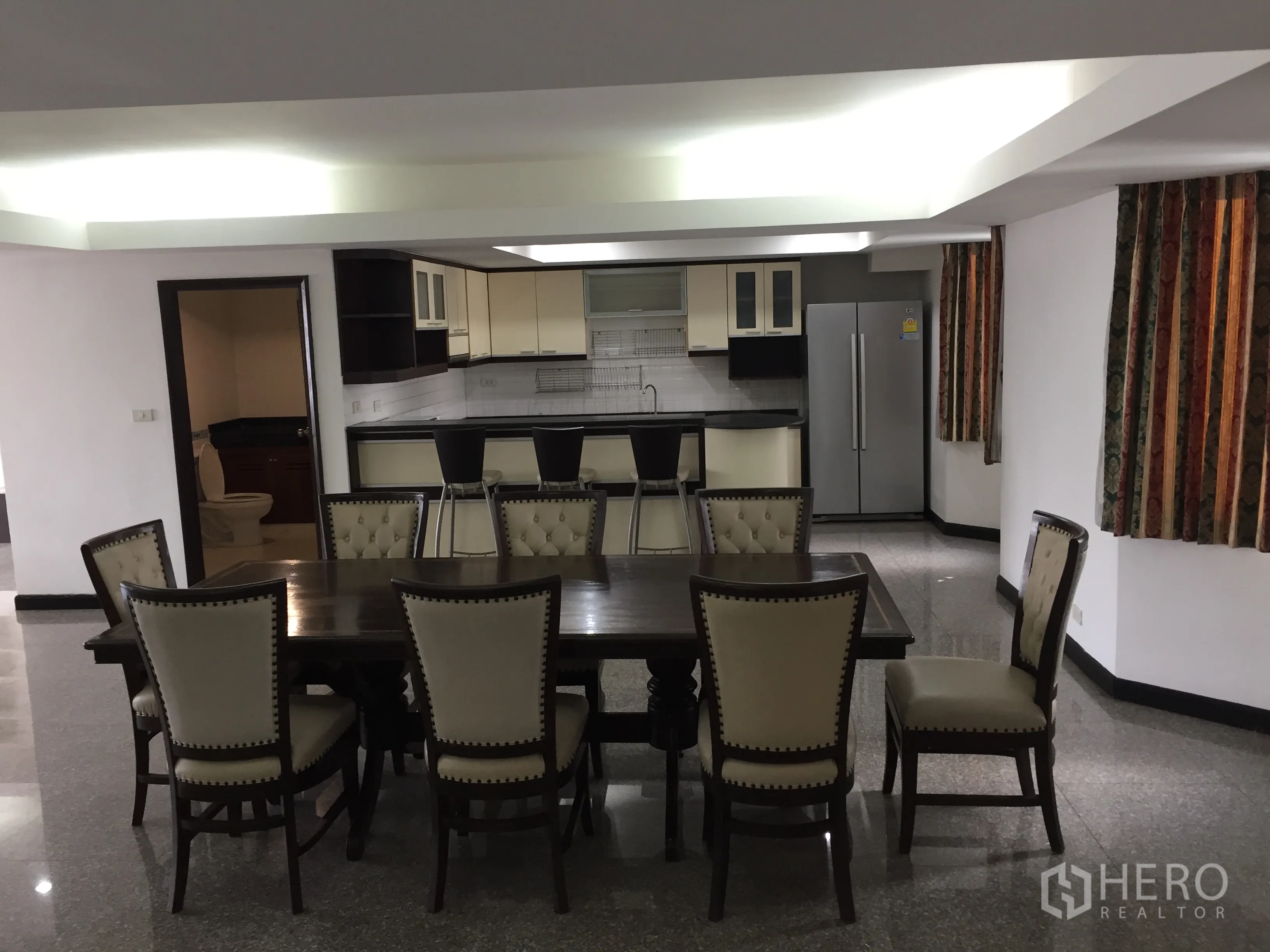 Condominium for rent in Watthana, Bangkok - Eight-seat dining table beside a breakfast bar and an open kitchen with modern cabinetry.