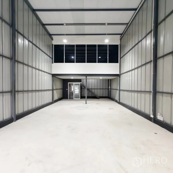 Warehouse for rent in Phra Khanong, Bangkok - High-ceiling warehouse interior with mezzanine glass office and smooth concrete flooring.
