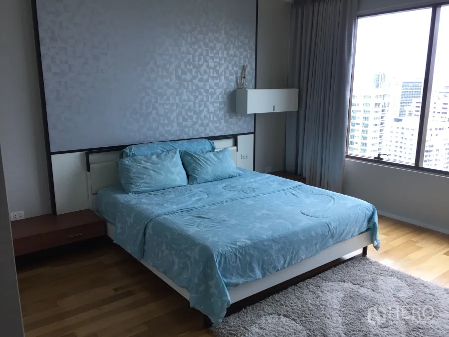 Condominium for rent or sale in Khlong Toei, Bangkok - Spacious master bedroom with blue bedding, wood floors and a large window overlooking the Bangkok skyline.