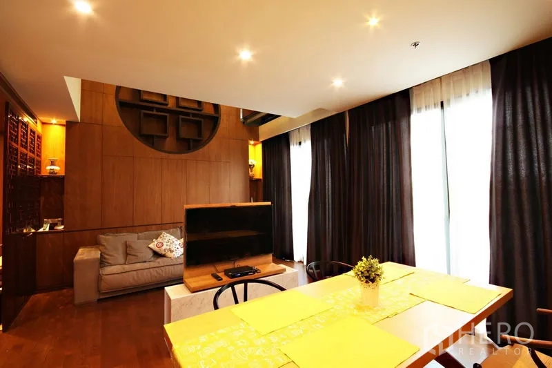 คอนโด ให้เช่าหรือขายในKhlong Toei, Bangkok - มุมนั่งเล่นอบอุ่นพร้อมโซฟา ชั้นวางทีวี ม่านสูงจรดเพดาน และผนังไม้เด่น