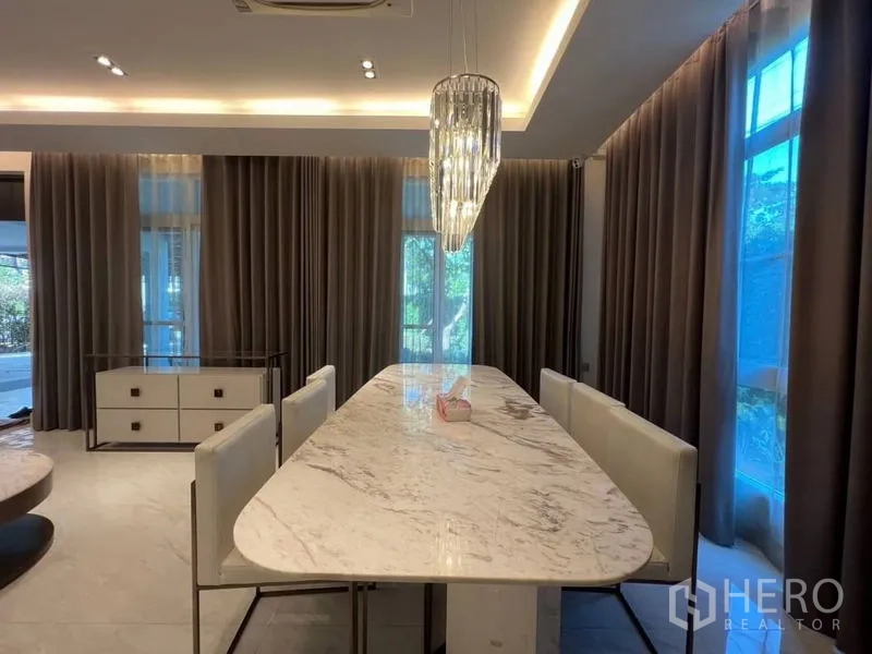 Detached House for rent or sale in Bang Phli, Samut Prakan - Dining zone with long marble table and crystal chandelier beside full-height windows.