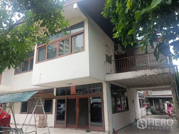 Detached House for rent in Bang Rak, Bangkok - Close-up of the house façade with large windows and a small upper balcony shaded by trees.