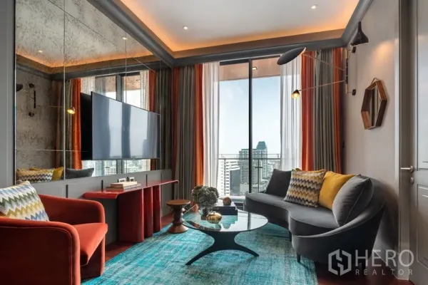 Condominium for sale in Watthana, Bangkok - Cozy lounge with wall‑mounted TV, teal rug, and balcony skyline view over Bangkok.
