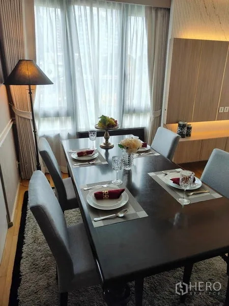 Condominium for rent or sale in Pathum Wan, Bangkok - Dining area set for four with tableware, rug, and a tall floor lamp beside a large window.