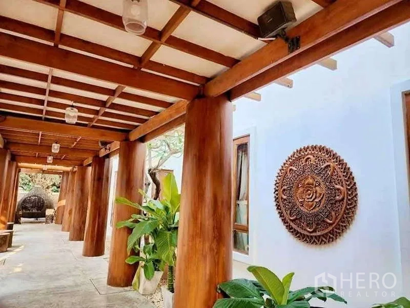 Detached House for sale in Bueng Kum, Bangkok - Covered wooden corridor with carved wall art and potted tropical plants.