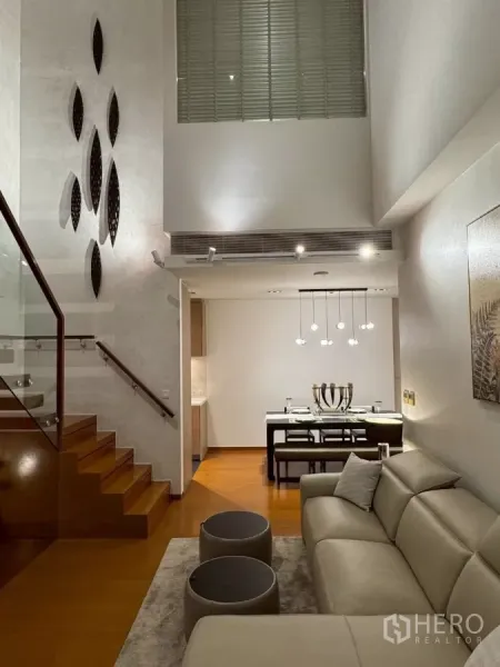 คอนโด ให้เช่าในSathon, Bangkok - ห้องนั่งเล่นและรับประทานอาหารเพดานสูงสองชั้น โคมไฟแขวน พร้อมบันไดไม้ราวกระจกในคอนโดหรูย่านสาทร