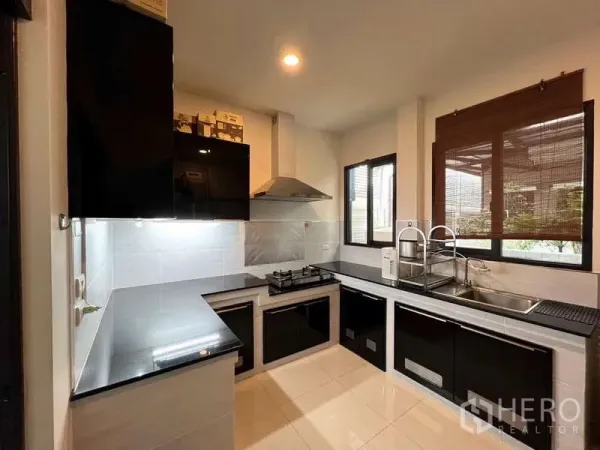 Detached House for sale in Prawet, Bangkok - Modern L-shaped kitchen with black gloss cabinetry, gas hob, range hood, and twin sinks by windows.
