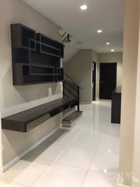 Detached House for rent in Thanyaburi, Pathum Thani - Hallway with floating console, geometric shelving, and a staircase leading upstairs.