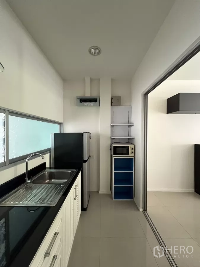 Townhouse for rent in Suan Luang, Bangkok - Galley kitchen with sink, fridge, and sliding door to the dining area.