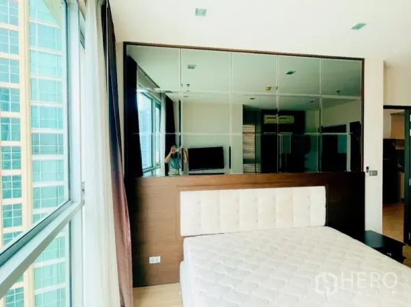 Condominium for rent - Bedroom corner with big window and mirrored wall panels reflecting the room.