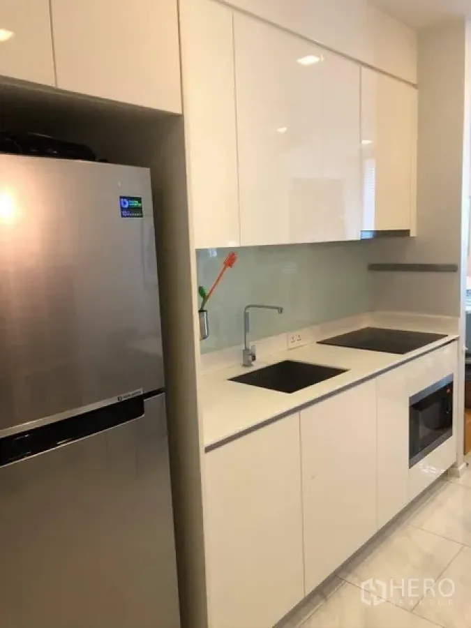 Condominium for rent or sale in Watthana, Bangkok - Compact white kitchen with glossy cabinets, induction hob, built-in oven and a stainless-steel fridge.