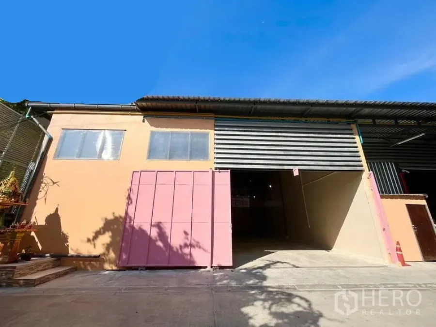 Warehouse for rent in Din Daeng, Bangkok - Warehouse exterior in Din Daeng with wide roller shutter and pink sliding gate under a high metal roof.