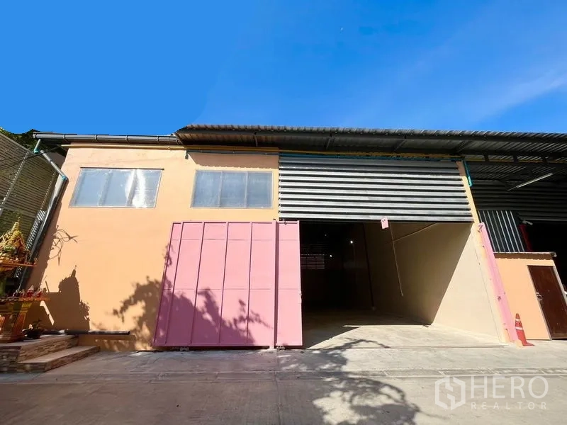 Warehouse for rent in Din Daeng, Bangkok - Warehouse exterior in Din Daeng with wide roller shutter and pink sliding gate under a high metal roof.