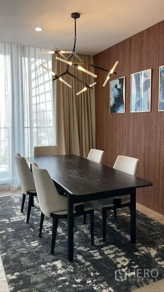 Condominium for rent in Pathum Wan, Bangkok - Dining area with dark wood table, beige chairs and designer chandelier on wood slat wall.